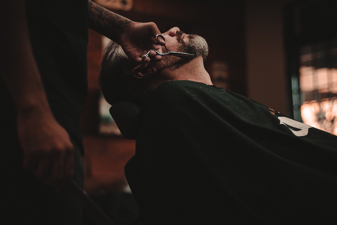 hombre sentado en barbería al que le cortan la barba con tijeras